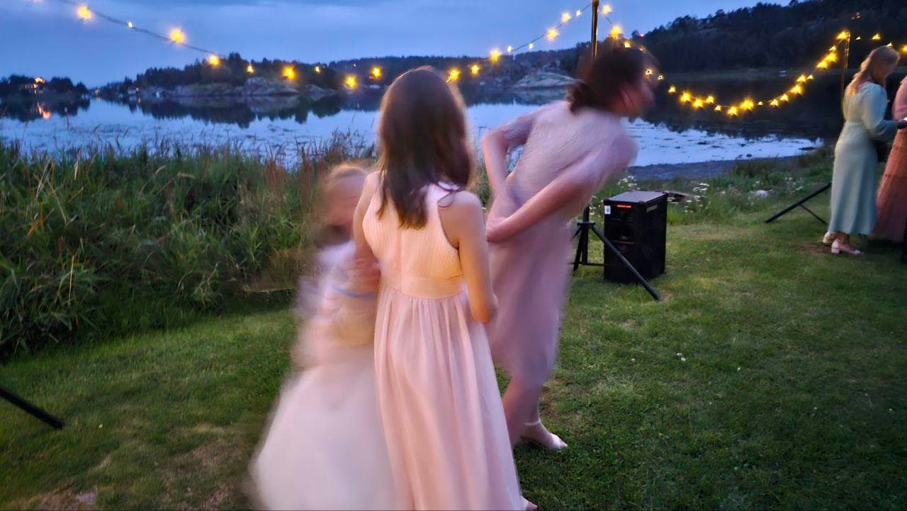 Gjester danser i hagen ved vannkanten med lyslenker og lysende dansegulv i bakgrunnen
